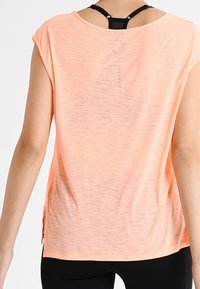 Camiseta atlética color melocotón con un ajuste holgado, mangas cortas y aberturas laterales. Presenta una tela texturizada y un detalle de ojal en la parte trasera.