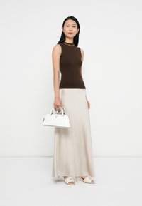 Bruine mouwloze top, beige maxi rok, witte handtas met zwarte accenten. Eenvoudig ontwerp met een gladde textuur en minimale patronen.