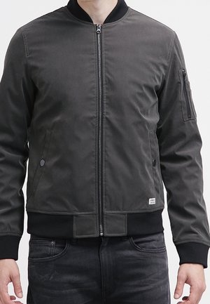 Dunkelgrau Bomberjacke mit einem Frontreißverschluss, geripptem Kragen und Bündchen, zwei Seitentaschen und einer Reißverschlusstasche am Ärmel. Glatte Textur.