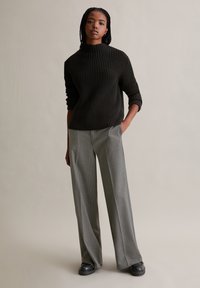 Schwarzer, strukturierten Strickpullover mit hohem Kragen, kombiniert mit grauen, gestreiften Palazzo-Hosen und klobigen schwarzen Schuhen.