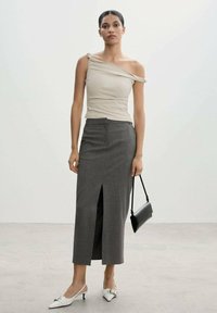 Top asimétrico beige, falda gris a rayas con una abertura hasta el muslo, combinada con zapatos slingback blancos y un pequeño bolso negro.