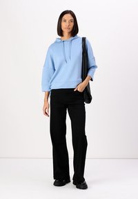 Felpa blu chiaro con cappuccio e maniche a tre quarti, dettagli con cordoncino laterale, abbinata a pantaloni neri a zampa e scarpe nere chunky.