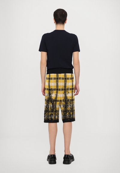 Navy short-sleeve t-shirt paired with yellow and black plaid shorts featuring a gradient design. Black shoes complete the outfit.