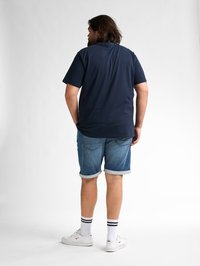 Navy polokošile s krátkým rukávem, džíny s ohrnutými manžetami, bílé tenisky a pruhované ponožky. Viditelný zadní pohled na volnočasový outfit.