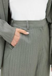 Hånd i lommen på grå stribede suitbukser brugt med matchende blazer og hvid top, vist fra taljen til midt lår.