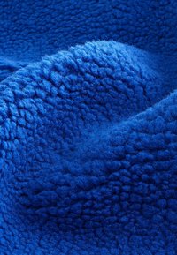 Gros plan d’un tissu polaire bleu doux et texturé avec des fibres surélevées et duveteuses et des plis légers créant des ombres et de la profondeur.
