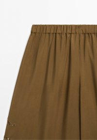 Brown skirt with elastic waistband and subtle embroidered detail on bottom left side against white background.