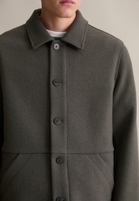 Donkergrijze, wollen jas met een kraag, zes knopen en zijzakken. Effen textuur met een gestructureerd ontwerp en minimale details.