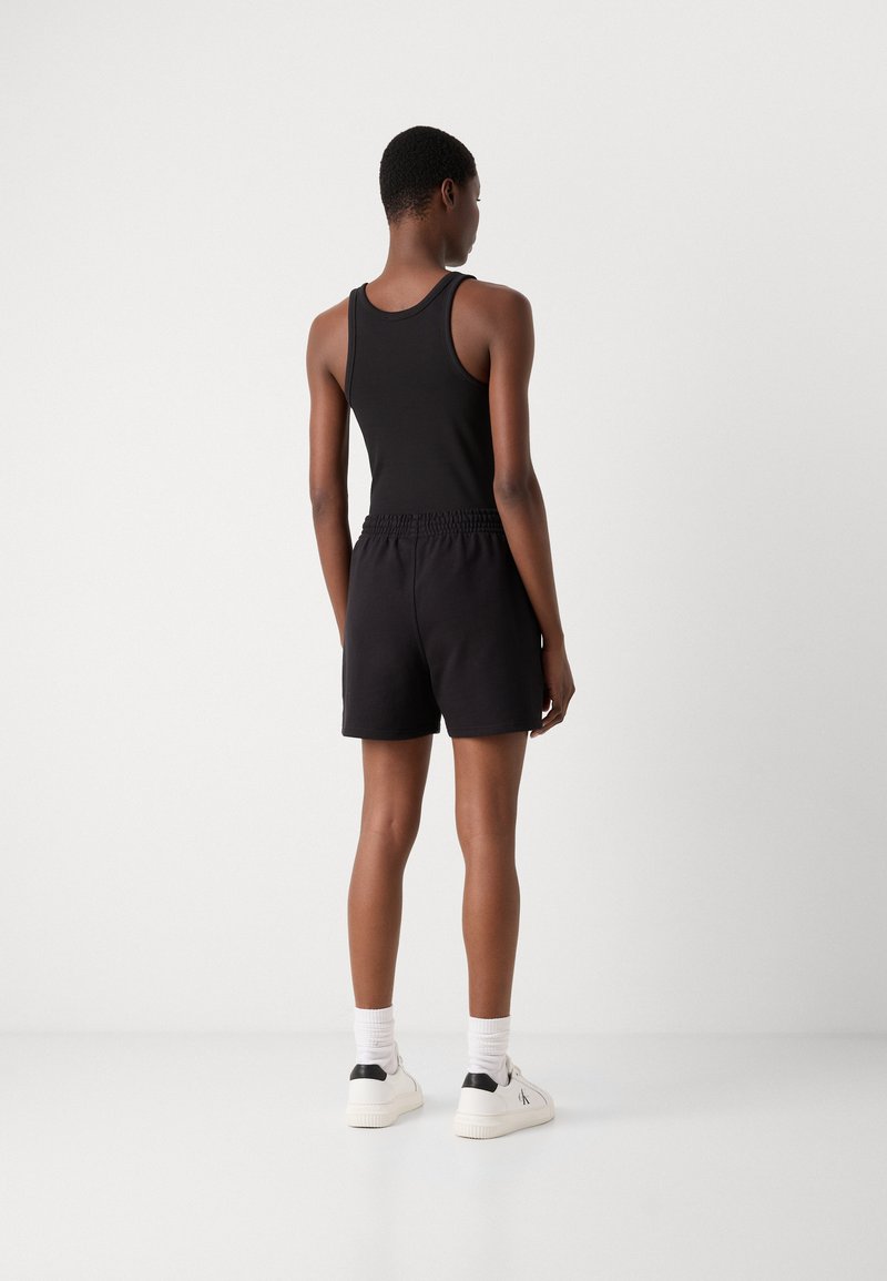 Zwarte tanktop en bijpassende zwarte shorts van een katoenmix, met een elastische tailleband. Model draagt witte sneakers met zwarte accenten.