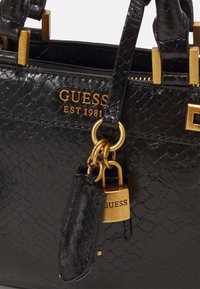 Mustat käsilaukut, joissa on teksturoidun keinokäärmeennahka viimeistely. Varustettu kultasävyisillä yksityiskohdilla, mukaan lukien padlock ja brändätty kirjain.