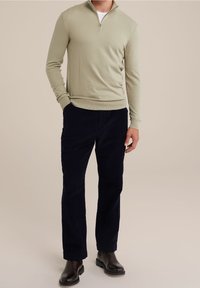 Pull-over vert clair avec un col à demi-fermeture éclair, associé  à un pantalon en velours côtelé bleu marine. La tenue est complétée par des bottes habillées noires.