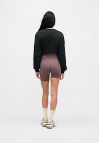 Μαύρο κοντό φούτερ, συνδυασμένο με μωβ σορτς ψηλής μέσης. Το μοντέλο φοράει μπεζ αθλητικά παπούτσια και κάλτσες κρεμ. Απλή, καθημερινή αθλητική εμφάνιση.