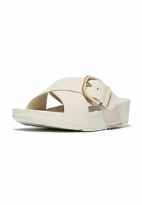 Sandalias de plataforma de color beige claro con un diseño de tiras anchas en cruz, suela texturizada y un acento de hebilla en tono dorado. Material de cuero sintético suave.