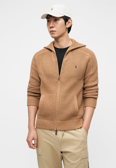 Καφέ πλεκτό πουλόβερ με φερμουάρ, με υφή στο σχέδιο, ριμπ μανσέτες και τελείωμα. Διαθέτει μικρό λογότυπο στην αριστερή πλευρά. Συνδυάζεται με μαύρο πουκάμισο.