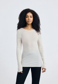 Lange mouwen, crèmekleurige top van een lichtgewicht, gestructureerd materiaal. Heeft een ronde halslijn en een aansluitend ontwerp, gecombineerd met zwarte leggings.