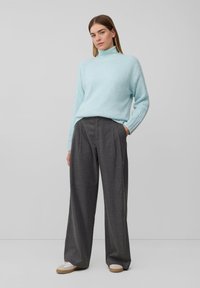 Pull à col roulé tricoté bleu clair associé à un pantalon large gris taille haute. Le modèle porte des baskets blanches avec des semelles beige.
