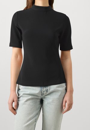 Czarny top z krótkim rękawem, o wysokim kołnierzu, prążkowanej teksturze i dopasowanym kroju, w zestawie z jasnoniebieskimi dżinsami.