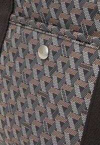 Gros plan d'une poche en tissu à motifs avec des formes géométriques et une texture pointillée, ornée d'un bouton argenté gravé "DARPOIS".