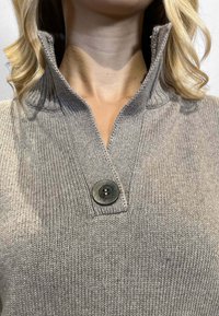 Pullover grigio a maglia con colletto pieghevole e un singolo bottone scuro. Il tessuto presenta una superficie liscia e una cucitura uniforme.