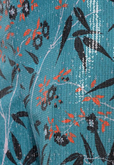 Tīrpu audums ar ziedu rakstu, kurā ir melni ziedi un sarkani akcenti, rotāts ar sekvīnēm, radot teksturētu virsmu.