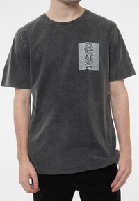 Gray cotton t-shirt with a crew neck, featuring a textured white graphic on the left chest area. Short sleeves and a relaxed fit.