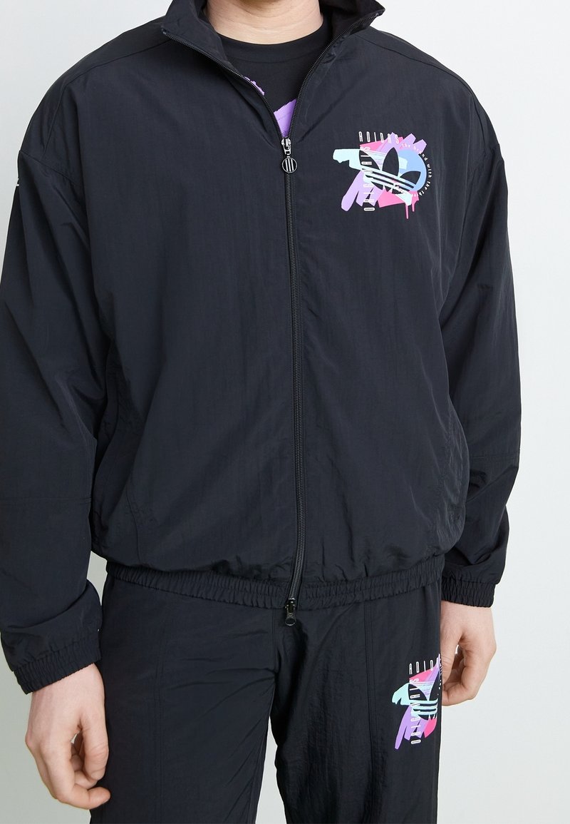 Svart vindjacka med dragkedja framtill, med färgglada grafiska detaljer och elastisk midja för en bekväm passform.