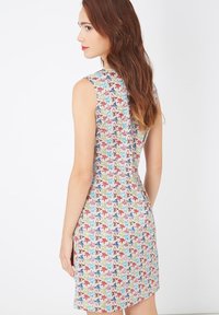 Vestido sin mangas de tela ligera con un vibrante patrón de hojas en tonos azules, verdes, rojos y marrones, con una silueta ajustada y hasta la rodilla.