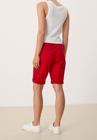 Pantalones cortos rojos enrollados hechos de tela ligera, con bolsillos traseros. Combinados con una camiseta de tirantes blanca ajustada y zapatillas blancas.