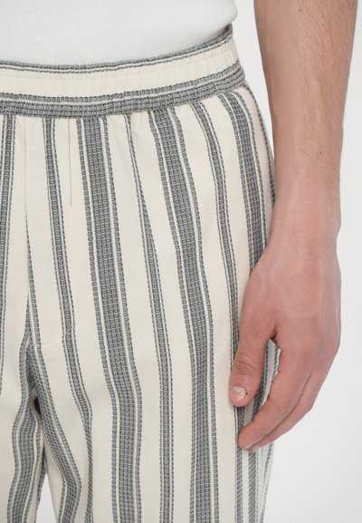 Striped pants featuring a lightweight fabric, elastic waistband, and vertical stripes in cream and gray. Close-up of hand on fabric.