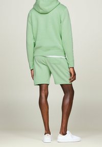 Felpa verde chiaro con tasca frontale, abbinata a pantaloni corti coordinati. Tessuto di media lunghezza e morbido, con dettagli di cucitura sottili e sneaker bianche.
