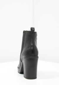Stivale ankle in pelle nera con punta arrotondata, finitura texturizzata e tacco a blocco alto. Presenta una linguetta e un sottile dettaglio di cucitura.