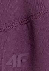 Gros plan sur un tissu violet avec des coutures renforcées et un logo « 4F » embossé sur le matériau.