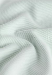 Tissu côtelé gris clair et doux avec de légers plis et de fines lignes de texture verticale créant un motif de surface lisse et fluide.