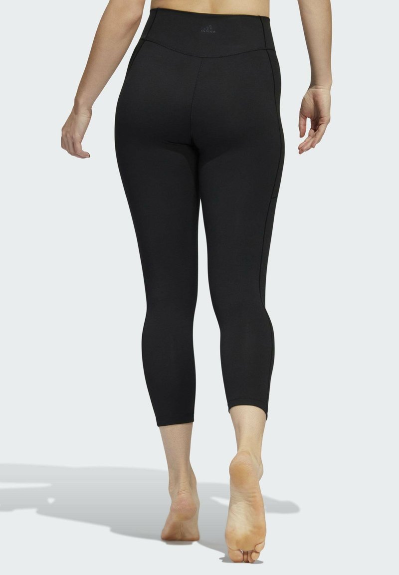 Leggings noirs ajustés avec taille haute, fabriqués en tissu extensible, présentant une texture lisse et des coutures minimales sur les côtés.