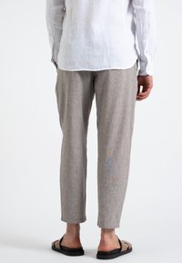 Jasnoszare lniane spodnie o luźnym kroju, zwężane nogawki i kieszenie po bokach, zestawione z czarnymi sandałami. Tkanina ma delikatną fakturę.