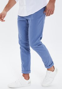 Chino blu chiaro con vestibilità affusolata, orli arrotolati, materiale in cotone, abbinati a sneakers bianche con dettagli grigi.