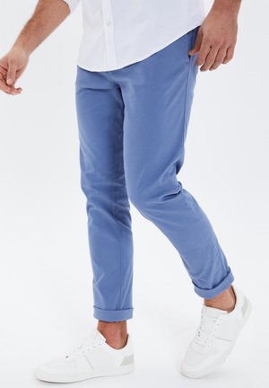 Chinos bleu clair avec une coupe fuselée, ourlets retroussés, en coton, associés à des baskets blanches avec des accents gris.