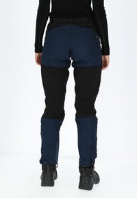 Waterdichte broek in marineblauw en zwart met een slank ontwerp, verstevigde knieën, een verstelbare taille en ritsen bij de boorden voor eenvoudig aan- en uittrekken.