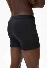 Schwarze Boxershorts aus glattem Stoff, mit einem engen, elastischen Bund und nahtlosem Design, das eine klassische Passform betont.