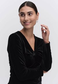 Svart sammetsblus med långa ärmar som har en v-ringning och en vriden knutdetalj fram, med rynkade ärmar och slät textur.