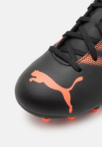 Cristian de fotbal negru cu o finisare texturată. Prezintă accente portocalii și un mare logo portocaliu Puma. Are șireturi negre și un vârf rotunjit.