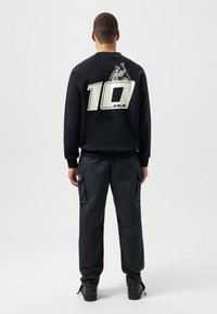 Sudadera negra con gran gráfico blanco "10" y texto "BALR." en la parte trasera, combinada con pantalones cargo gris oscuro que cuentan con múltiples bolsillos.