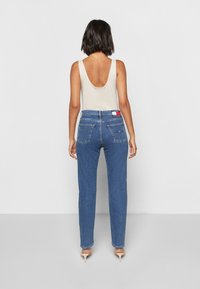 Light beige tank top with a low back, paired with medium blue denim jeans featuring a high waist and two back pockets.