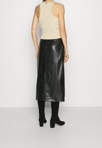 Musta nahkainen midi-hame, jossa on sileä pinta, takana halkio ja minimimäärä saumoja, yhdistettynä istuvaan beigeksi ribbikuvioituun toppiin.