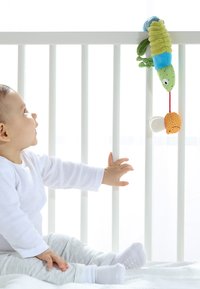 Jouet en peluche de chenille coloré avec plusieurs textures et motifs, suspendu au-dessus d'un bébé qui tend la main, entouré d'un fond clair.