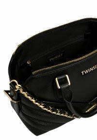 Borsa a tracolla in pelle nera con superficie testurizzata, dettagli in metallo dorato, tasca interna con cerniera e tracolla a catena.