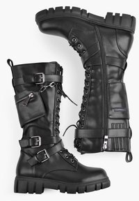 Botas de combate de cuero negro con sujeción de cordones en la parte delantera, hebillas, cremalleras y detalles de tachuelas. Suelas de goma gruesa para mayor tracción.
