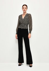 Blusa nera a fantasia con maniche lunghe e puffate, con cintura arricciata, abbinata a pantaloni neri a vita alta e svasati e tacchi a punta.