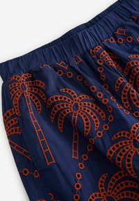 Marine stof med livlig orange broderi af palmer. Har elastisk talje, indviklede mønstre og tekstureret detaljering overalt.