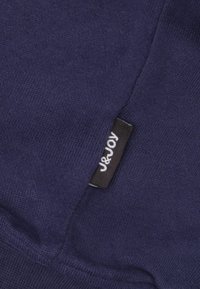 Marineblauwe tricotstof met een gladde textuur, met een zwart label waarop "J&Joy" op de zijkant is gestikt. Eenvoudig en onopvallend ontwerp.